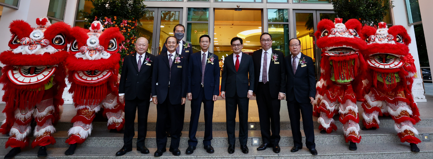 Group of men in suits pose with two red Chinese lion dance costumes in front of a building.
